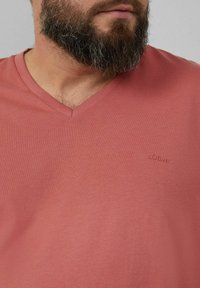 Kurkelnähe, kurzärmeliges T-Shirt aus korallenfarbenem Baumwollstoff mit glatter Textur. Verfügt über ein dezentes, auf die Brust gesticktes s.Oliver-Logo.