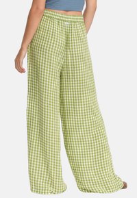 Gröna rutiga vida byxor med elastisk midja. Tyget är lätt och har en subtil textur, med ett gingham-mönster.