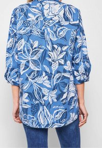 Blue floral shirt made of lightweight fabric with a loose fit. Features white floral patterns, roll-up sleeves, and a curved hem.
