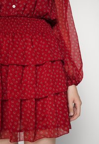 Abito rosso a strati realizzato in tessuto leggero, con un motivo floreale, vita elastica e lunghe maniche trasparenti con polsini arricciati.