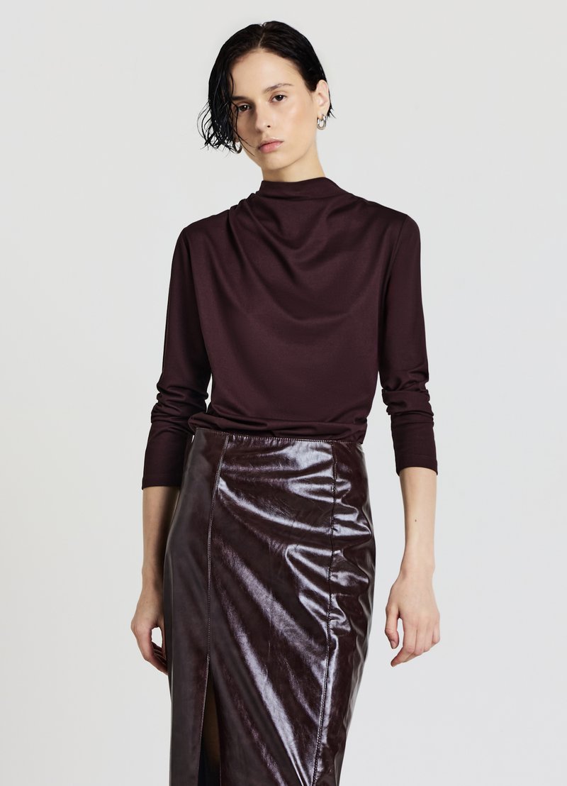 Haut bordeaux à manches longues avec un col drapé, associé à une jupe en cuir brillant taille haute avec une fente à l'avant.