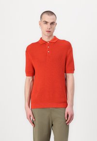 Rød kortermet polo-skjorte med strukturert strikkemønster, med klassisk krage, tre knapper og ribbestrikkede mansjetter, paret med olivengrønne bukser.