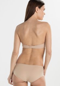 Nude bikiniset med et strapless topp og midt-høy bukser. Glatt stoff med minimalt design og lukking bak.