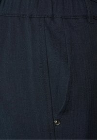 Dark blue herringbone fabric featuring a side pocket and a metal button detail. The texture is smooth with a subtle pattern.