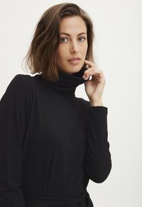 Svart polokrage topp i mjukt material, med långa ärmar och en avslappnad passform samt ett knytbälte i midjan.
