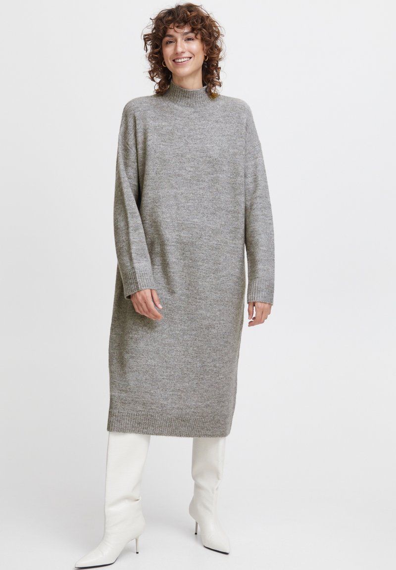 Vestido de punto gris con un escote alto, mangas largas y puños acanalados. Combinado con botas blancas hasta la rodilla para crear contraste.