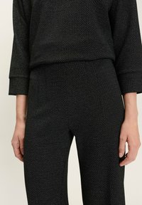 Tenue noire texturée comprenant un haut ample et un pantalon ajusté, avec un motif tissé subtil et des détails en fil contrastant.