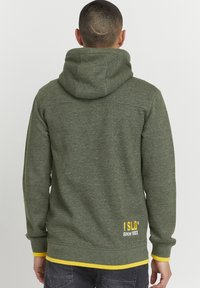 Green hoodie featuring a textured fabric, a large hood, yellow accents at the cuffs and hem, and embroidered logo on the back.