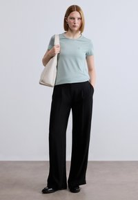 Ανοιχτό μπλε κοντομάνικο μπλουζάκι, μαύρο παντελόνι με φαρδιές πατούρες, κρεμ τσάντα, μαύρα παπούτσια, με ένα μικρό λογότυπο στο στήθος του μπλουζιού.