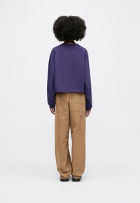 Purple cropped sweatshirt with long sleeves, paired with loose beige cargo pants. Smooth texture, minimal detailing, functional pockets on pants.