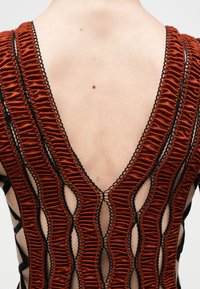 Πλάτη που δείχνει φόρεμα με βαθύ V ντεκολτέ, με εναλλασσόμενα κάθετα βολάν σε σκουριά απόχρωση και μαύρα δίχτυα που αποκαλύπτουν το δέρμα.