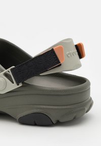Sandale verte et grise avec une sangle noire, arborant un design texturé et des accents orange sur le fermoir de la sangle et la semelle.