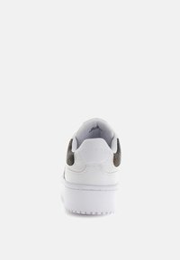 Sneaker bianco con dettagli in rilievo marrone sul tallone, suola piatta, cuciture decorative e logo del marchio impresso sul retro.