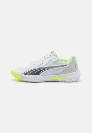 Zapatilla deportiva blanca con acentos en verde neón, talón gris y franja lateral negra. Presenta una parte superior de malla transpirable y suela de goma con patrón.