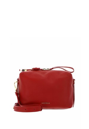 Sac bandoulière en cuir rouge avec sangle réglable, ferrures dorées, fermeture éclair et logo "Coccinelle" sur le devant.