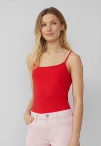 Rode tanktop van rekbaar materiaal, met dunne bandjes en een ronde halslijn, gecombineerd met lichtroze jeans.