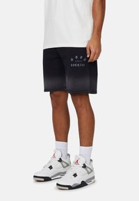 Pantaloni corti neri con una stampa di testo grigia, abbinati a scarpe da ginnastica bianche e grigie. Il testo recita "NON DIMENTICARE NULLA."