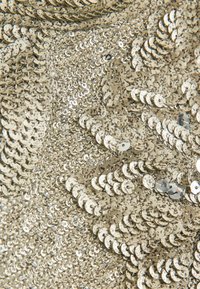Gold sequined fabric featuring numerous small, round sequins reflecting light, layered to create texture and shine with subtle patterns.