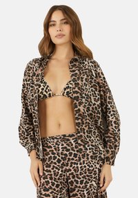 Camicia a bottone con stampa leopardata, tessuto leggero, vestibilità over size, con top bikini e pantaloni coordinati, caratterizzata da diverse fantasie marroni e nere.