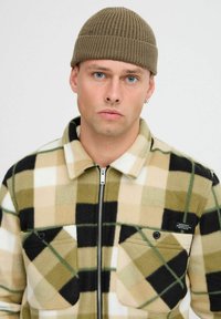 Veste en polaire à carreaux beige, vert et noir. Présente un col, une fermeture zippée à l'avant, deux poches poitrine et une petite étiquette de marque.