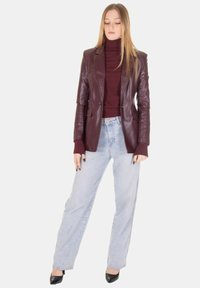 Blazer in pelle bordeaux sopra un dolcevita bordeaux aderente, abbinato a jeans a gamba larga azzurri e tacchi neri. Tessuto liscio, vestibilità sartoriale.