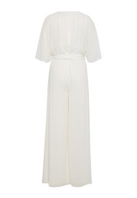 Fehér overall övvel a derekán, rövid áttetsző ujjak és laza szabás. Puha, könnyű anyag elegánsan omlik le a hátról.