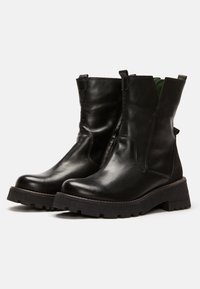 Botas de tobillo de cuero negro con punta redondeada, lados texturizados y suela de goma gruesa. Incluyen tiradores para facilitar su uso.