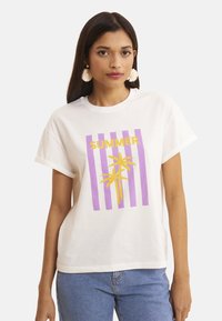 Camiseta blanca de algodón con un diseño de rayas moradas y texto amarillo que dice "VERANO" acompañado de un gráfico de una palmera. Manga corta, corte relajado.