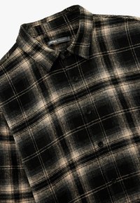 Schwarz-beige karierte Flanellhemd mit langen Ärmeln, Knopfleiste, klassischem Kragen und schwarzen Plastikknöpfen. Weiche Textur. Normale Passform.