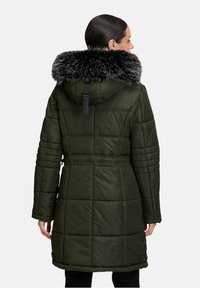 Oliwkowy puchowy płaszcz z odpinanym czarnym futerkiem z sztucznego materiału, wyszczuplonym w pasie i pikowany. Posiada średnią długość i długie rękawy.