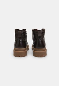Stivali alla caviglia in pelle nera con finitura liscia, suola in gomma marrone e zip sul retro. Presentano una linguetta per un facile indossamento.
