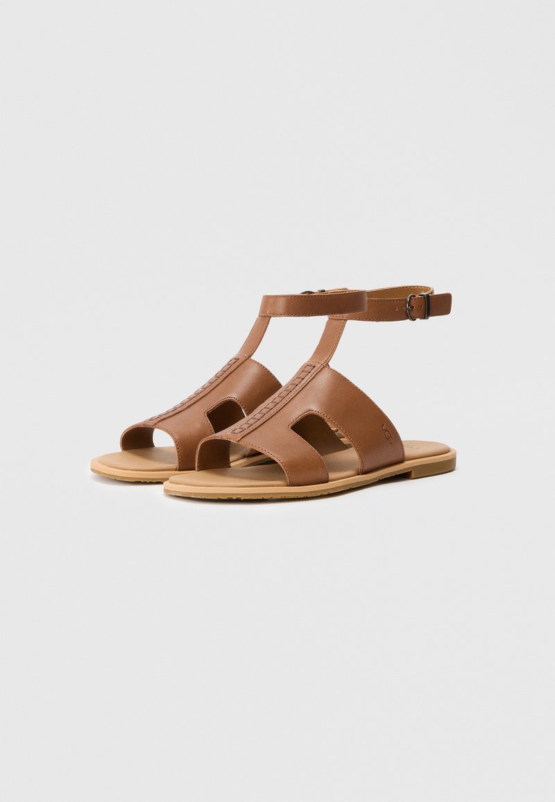 Bruine leren sandalen met open tenen en T-band ontwerp, voorzien van een gesp sluiting en een platte zool, met intrigerende stikdetails.