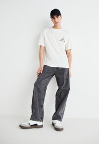 White cotton t-shirt featuring a small printed triangle design, paired with high-waisted black denim pants, and white sneakers with black accents.