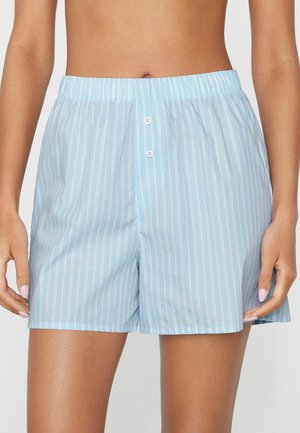 Jasnoniebieskie szorty z białymi pionowymi paskami, elastycznym pasem i dwoma przednimi guzikami, noszone przez osobę z rękami swobodnie opuszczonymi wzdłuż ciała.