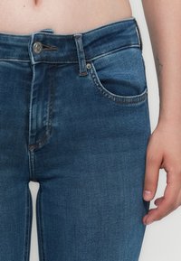 Smarte blå denimjeans med en frontlomme, metallknaplukning og kontraststing. Stoffet har en glat, let falmet tekstur.