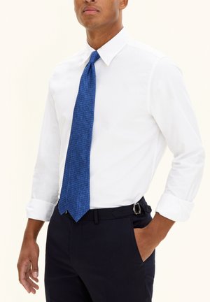 Weißes Hemd mit blauem gemustertem Krawatte, kombiniert mit dunklen marineblauen Hosen. Die Krawatte hat ein strukturiertes Design und einen zulaufenden Ende.