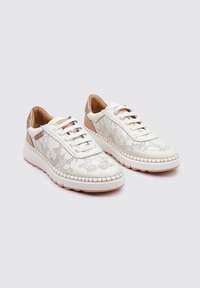 Zapatillas blancas con parte superior perforada, acentos en beige y suela de goma texturizada. Presenta cordones y costuras decorativas a lo largo del borde.