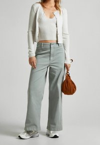 Vaaleanharmaat leveälahkeiset housut, joissa on korkea vyötärö, yhdistettynä valkoiseen ribbikuvioiseen croppikardigaaneen ja ruskeaan mokkalahjakäsiin. Teksturoidut kankaat näkyvät hyvin.