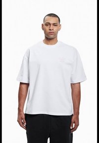 White cotton t-shirt with short sleeves, loose fit, crew neckline, and small pink text detail on the left chest area.