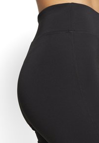 Czarne legginsy z wysokim stanem, wykonane z elastycznego materiału, z płaskimi szwami, gładką teksturą i bez widocznych wzorów czy detali hardware.
