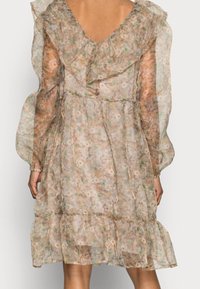 Robe en tissu léger à imprimé floral beige avec des manches à volants et un ourlet volanté. Elle présente un dos en V et des poignets élastiques.