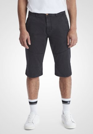 Svart knelang shorts laget av slitesterk bomull, med rett snitt, frontlommer og synlige sømmer på bena.