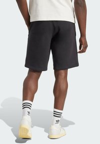 Shorts en coton noirs avec une coupe mi-cuisse, dotés d'une taille élastique. Portés avec des baskets blanches et des chaussettes rayées. Design simple.