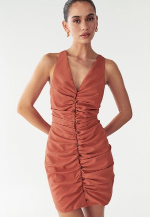 Haljina u rust boji bez rukava s dubokim V-izrezom, nabrano detaljisanje i ukrasni gumbi duž prednje strane. Glatka, mekana tekstura tkanine.