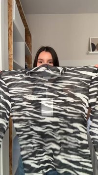 Άτομο κρατάει μία μακρυμάνικη μπλούζα με ασπρόμαυρες ρίγες ζέβρας και μια λευκή κενή ετικέτα σε έναν μινιμαλιστικό χώρο.