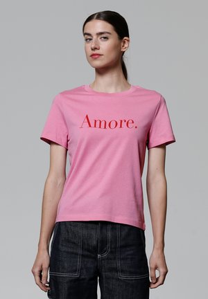 T-shirt en coton rose avec le mot "Amore." en lettres rouges en gras. Manches courtes, col rond et coupe décontractée.