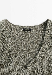 Cardigan grigio e crema lavorato a maglia con scollo a V, caratterizzato da un tessuto testurizzato e una chiusura con un singolo bottone nero davanti. Etichetta visibile all'interno.