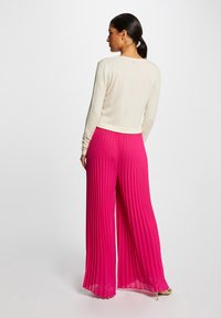 Calças largas e plissadas em tom rosa com um design fluido, combinadas com uma blusa justa de manga longa em creme. Textura suave e ajuste descontraído.