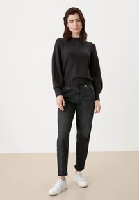 Zwarte gebreide trui met brede mouwen, gecombineerd met losse, donkere jeans en witte sneakers. De textuur is zacht en glad.