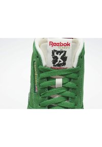 Zelený semišový teniska se zelenými tkaničkami, štítek Reebok Classic a grafika Human Rights Now na jazyku.